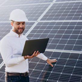 Young architect standing by solar panels making diagnostics on computer